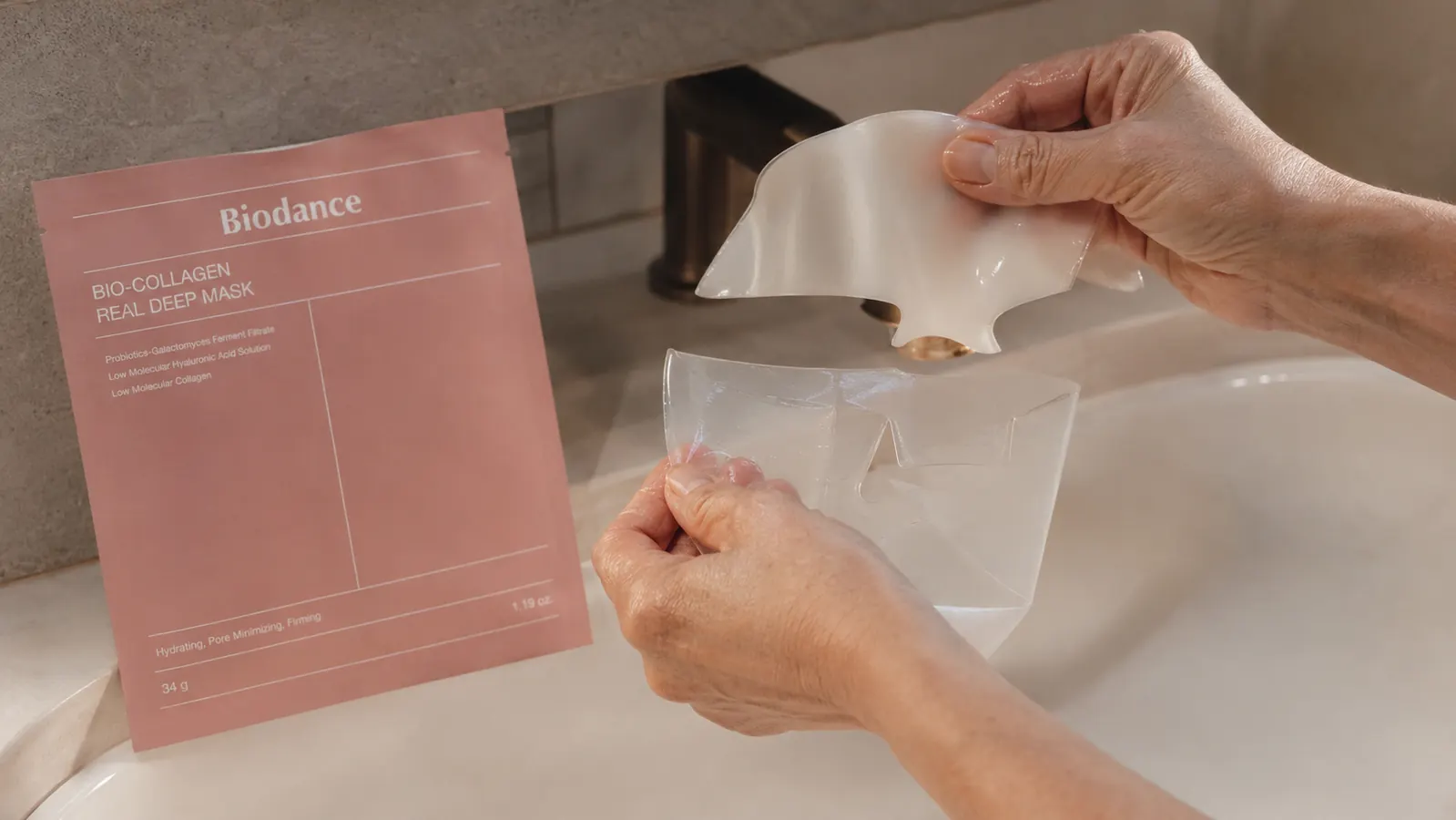 A woman's hands peeling a two-piece hydrogel mask apart before smoothing the bottom half onto her jawline