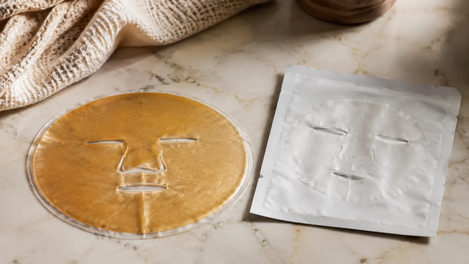 Two skincare masks side by side on a bathroom counter, a hydrogel overnight mask and a folded paper sheet mask, soft morning light