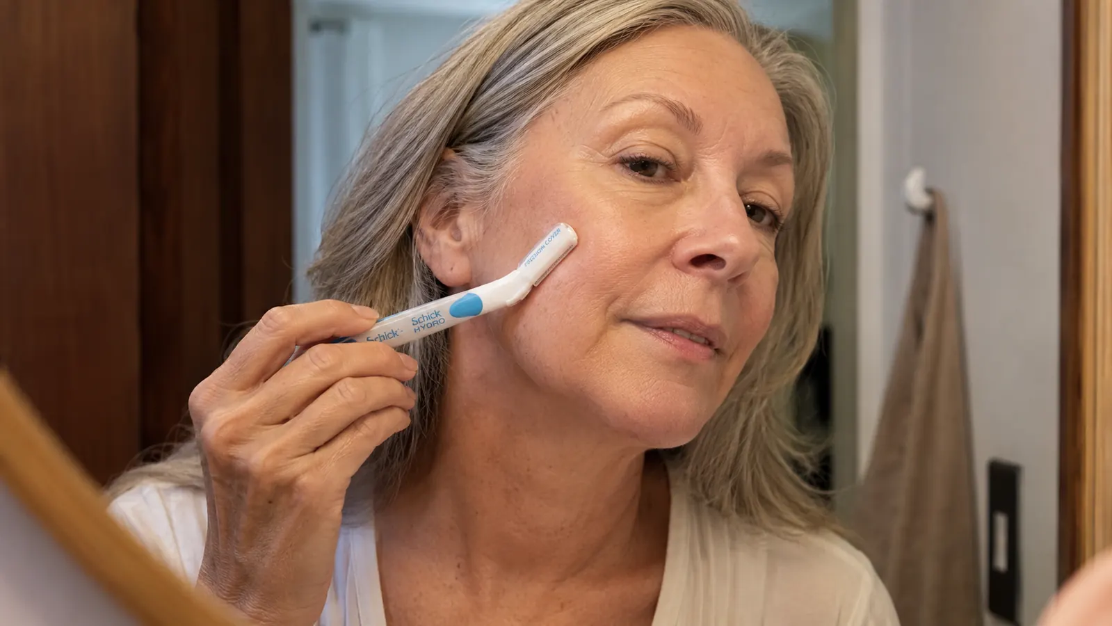 Close-up of a hand holding the Schick Hydro Silk dermaplaning tool at a low angle against a cheek, demonstrating the correct stroke angle