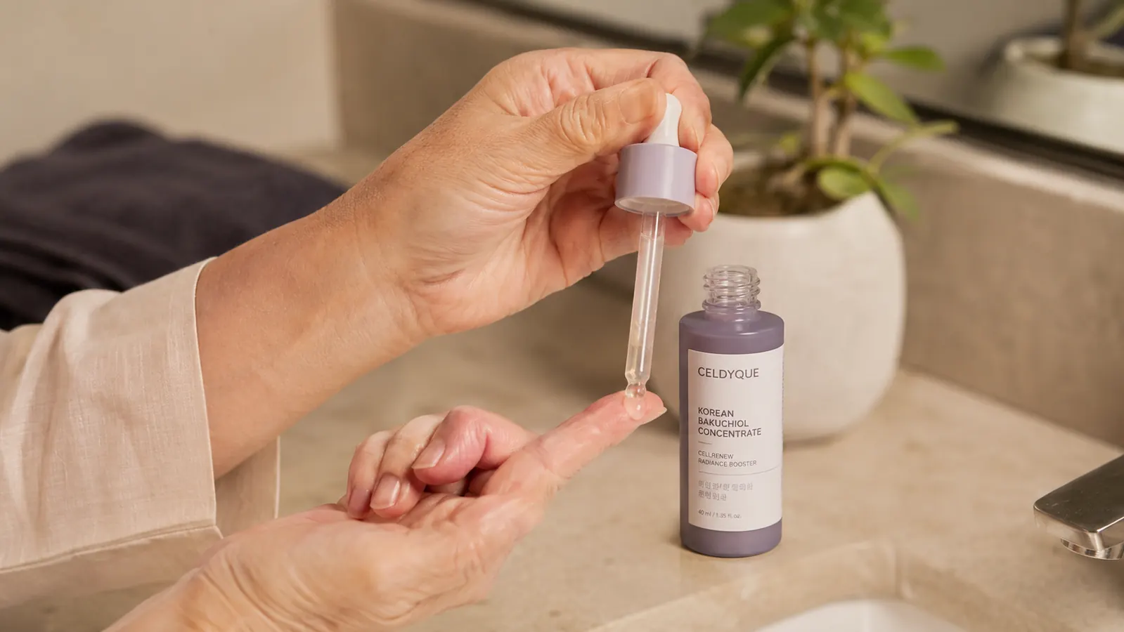 Hand holding a dropper of bakuchiol serum with a single drop suspended above fingertips